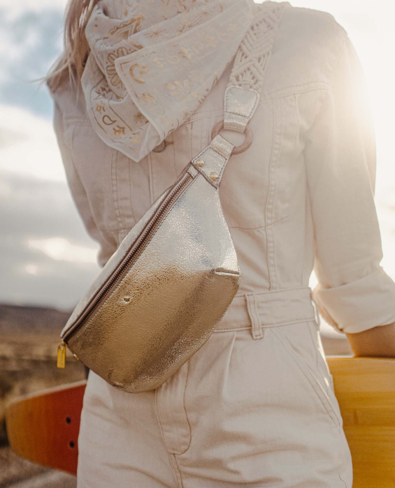 Sac banane en cuir doré porté par une femme dans une combinaison blanche