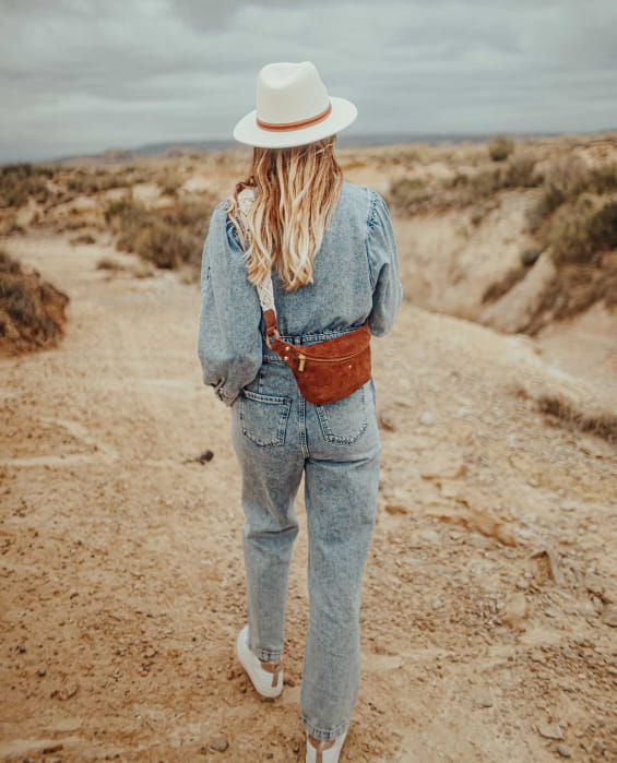 Femme marchant dans le désert avec un sac banane et un chapeau en feutre